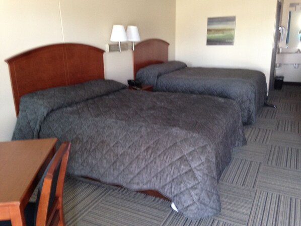 A hotel room with two beds, a desk, a chair, a lamp, and a painting on the wall. - Crossroads Lodge (Pender)