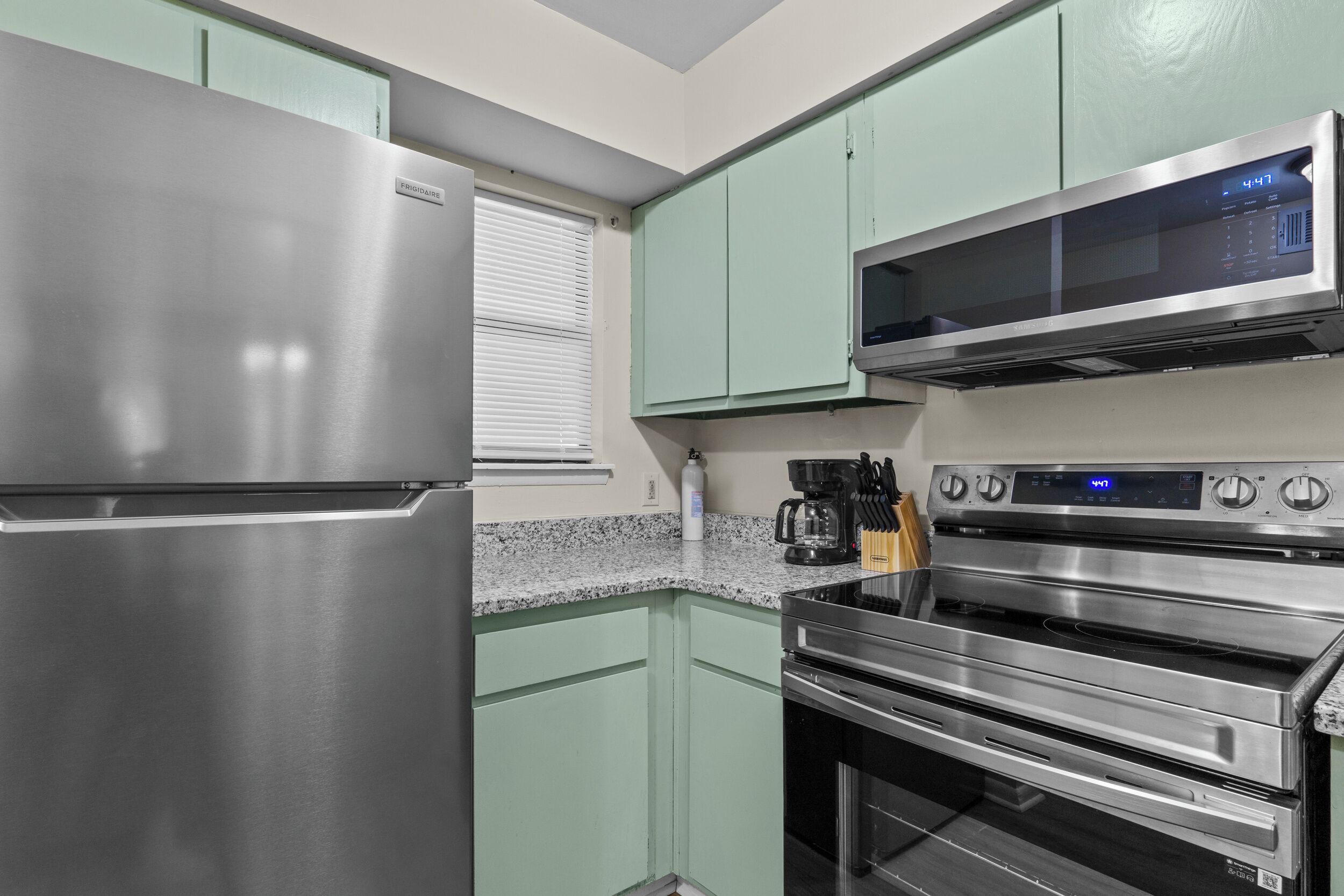 A kitchen with stainless steel appliances, green cabinets, and a microwave above the oven.