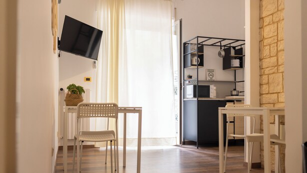 Une cuisine moderne dotée d’un téléviseur à écran plat fixé au mur, d’un coin repas avec une table et des chaises, et d’un îlot de cuisine équipé d’un évier et d’étagères de rangement.