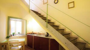 A kitchen with a dining table and chairs, a window with plants, and a staircase with a glass railing. - CHARMING ROOFTOP FLAT IN CITY CENTER (Catania)