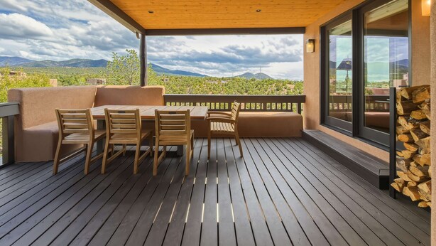 Ein überdachter Außenbereich mit Tisch und Stühlen, einer Holzterrasse und Blick auf eine gebirgige Landschaft.