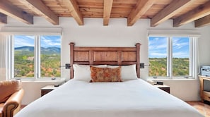 A bedroom with a wooden headboard, a large bed, two nightstands, a chair, and a view of a mountainous landscape through large windows. - Casa de Azulejos (Santa Fe)