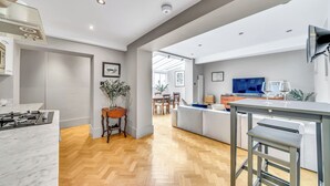 Et moderne køkken med en marmorbordplade, plankegulv i fiskebensmønster og en central ø med barstole.