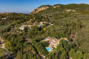 Vista aérea de Villa Koumquat rodeada de vegetación densa y colinas.
