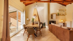 A cozy living area with a wooden ceiling, a dining table with chairs, a sofa, and a fireplace. - Villa Koumquat by Villa Plus (Paleokastritsa)