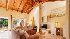 A spacious living room with a brown sofa, a TV, and a dining area with a table and chairs. - Villa Koumquat by Villa Plus (Paleokastritsa)