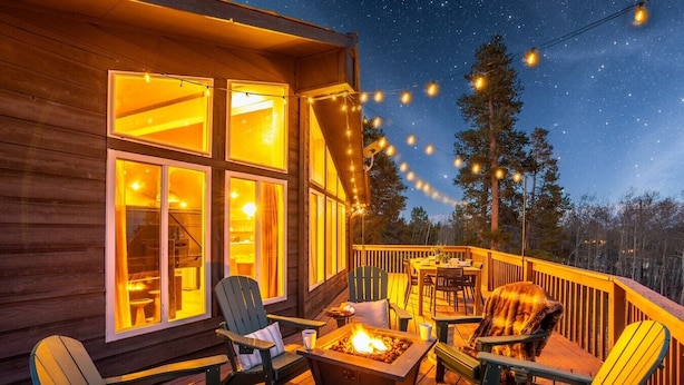 Un patio in legno con posti a sedere all'aperto, un braciere e luci decorative appese sotto un cielo notturno.