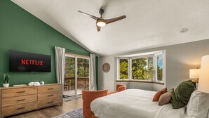Una camera da letto con un letto, una televisione, una ventola a soffitto, una cassettiera, una finestra e un balcone.