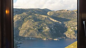 A window view of a mountainous landscape with a lake and buildings on the hills. - Taenarioum Antico - Mani Stone Tower With Sea View (East Mani)