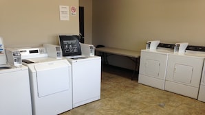A laundry facility with washers and dryers, a bench, and a caution sign on the wall. - Logan Creek Inn (Randolph)