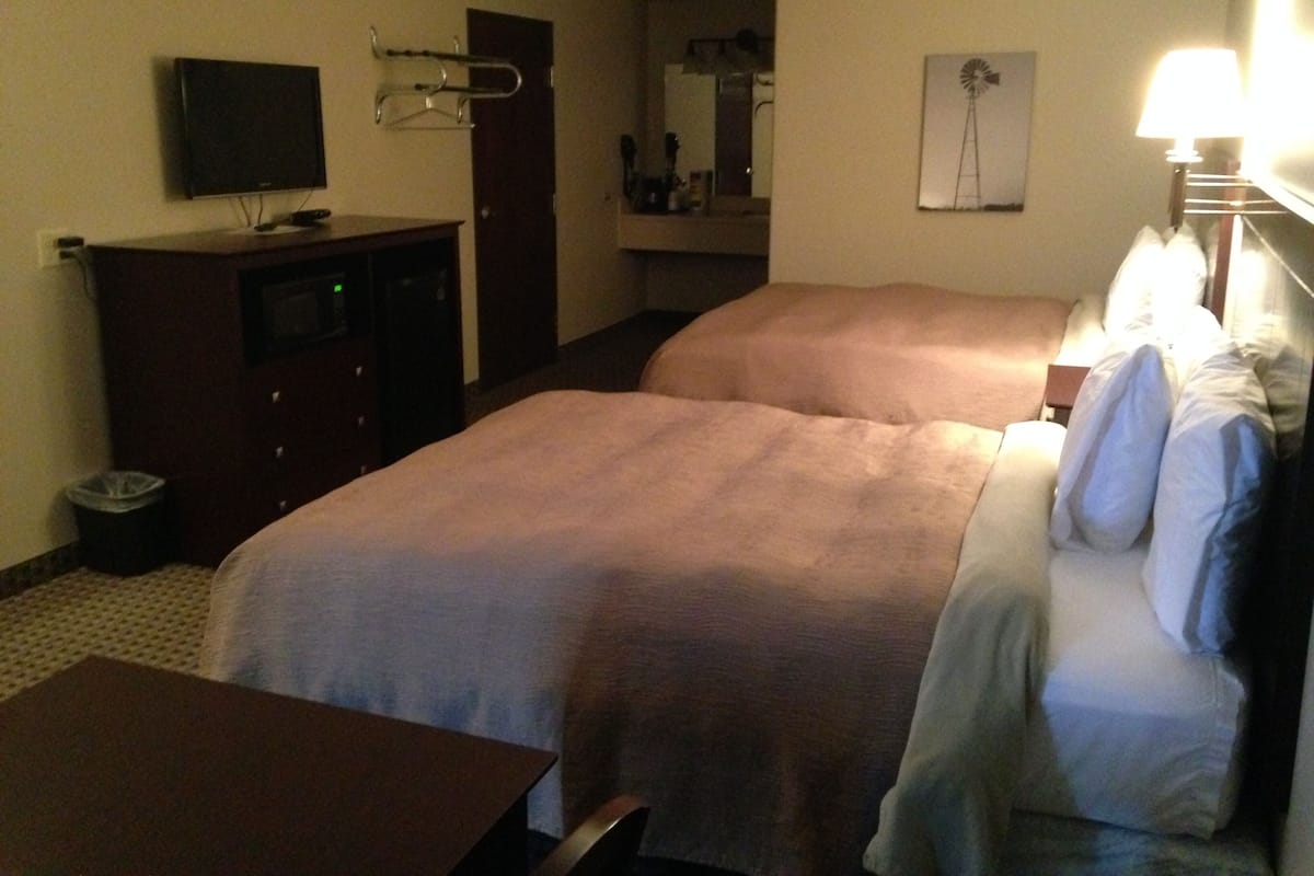 A hotel room with two beds, a TV, a desk, and a mirror.