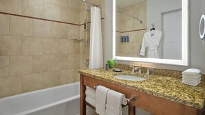 Ein Badezimmer mit Badewanne, einem Waschbecken mit Granitarbeitsplatte, einem Spiegel und einer Dusche mit gebogener Glastür.