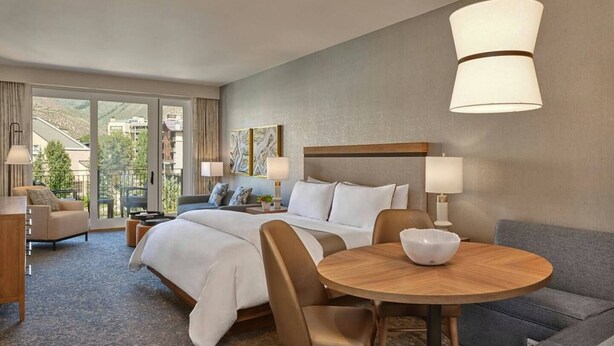 Ein Hotelzimmer mit einem großen Bett, einem runden Esstisch, einer Couch und einem Balkon mit Bergblick.