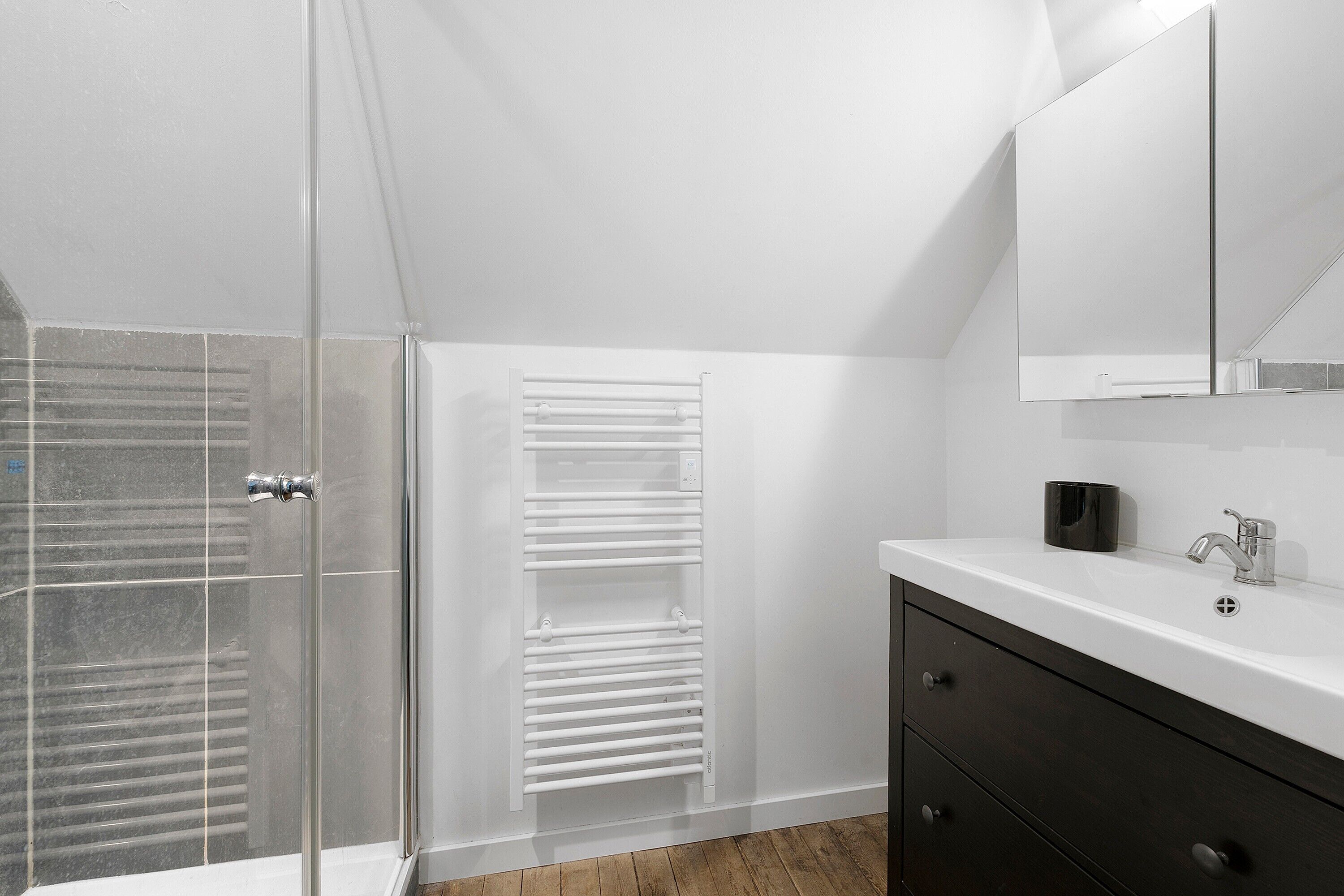 Une salle de bain moderne avec une douche à parois de verre, un meuble-lavabo blanc avec un miroir et un porte-serviettes.