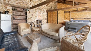 A rustic interior with stone walls, wooden beams, wicker furniture, and a kitchenette.