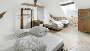 A bedroom with a sloped ceiling, a wooden wardrobe, a stone wall, and a bed with white bedding.