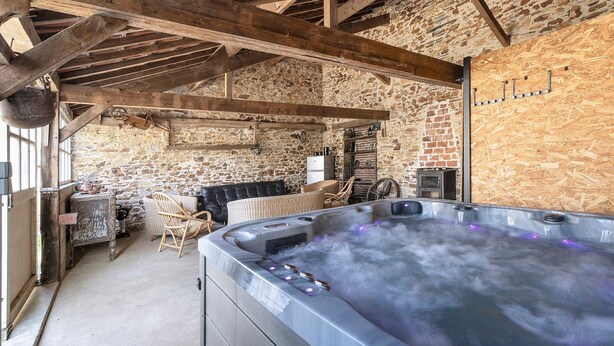 A rustic stone interior with a hot tub, wooden beams, and a brick wall.