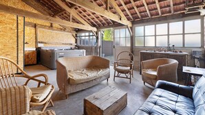 A rustic interior with exposed wooden beams, wicker furniture, and a view through large windows.