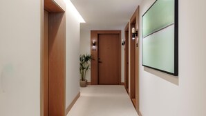A hallway with wooden doors, a potted plant, and a wall-mounted screen. - Fulham Pier Hotel (London)