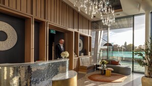 A modern reception area with a reception desk, seating, and a large window offering a view of the outdoors. - Fulham Pier Hotel (London)