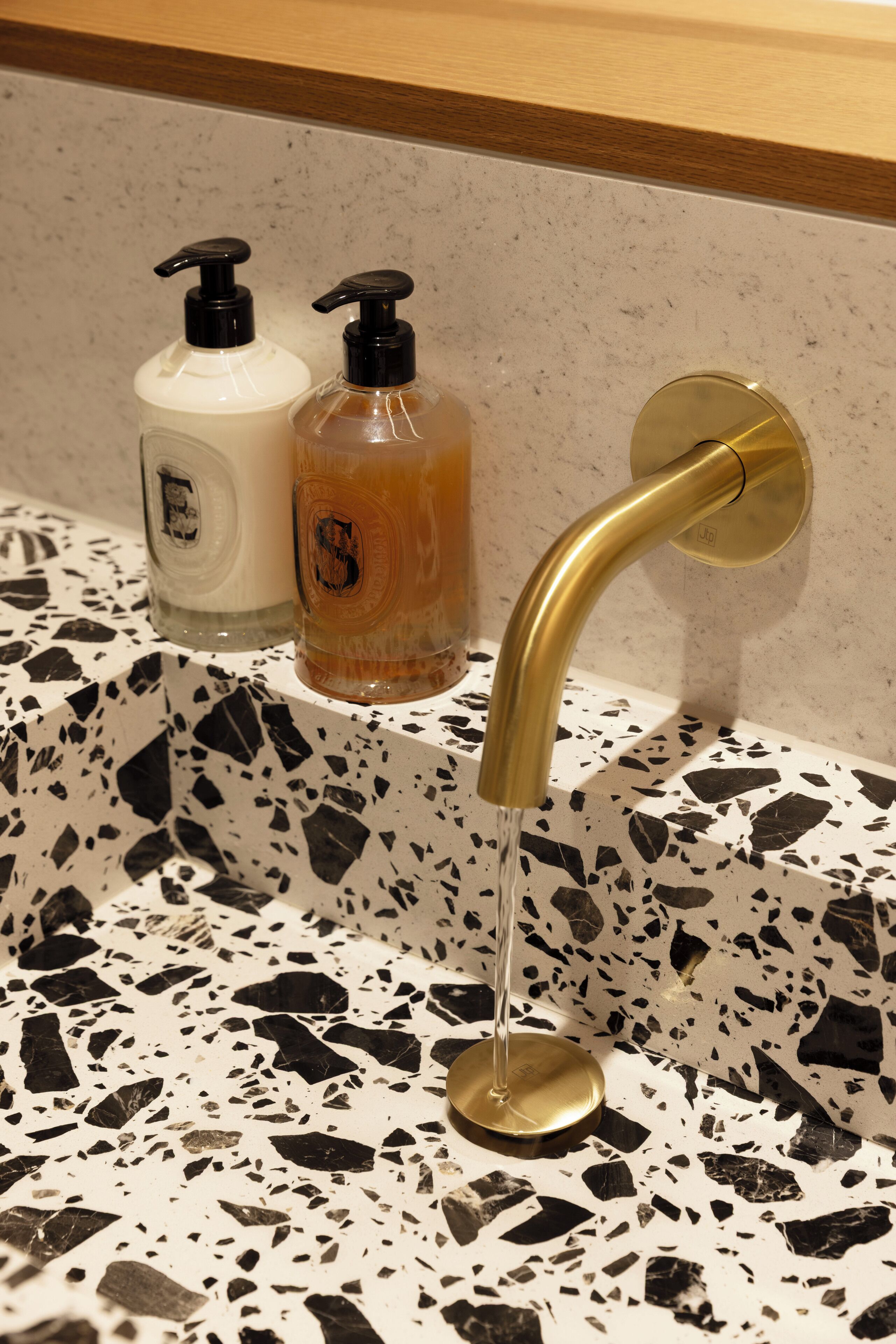 Een wastafel met een gouden kraan, twee zeepdispensers en een bezaaid aanrecht.
