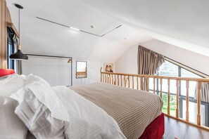 Un dormitorio con cama, una lámpara colgante, ventilador de techo, un cuadro y vistas al exterior.