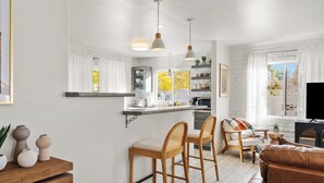 A modern kitchen with white cabinets, a bar area with wooden stools, a sofa, and a television. - LOCATION! Uptown Retreat HotTub, Mini Putt, Fire Pit & Views (Sedona)