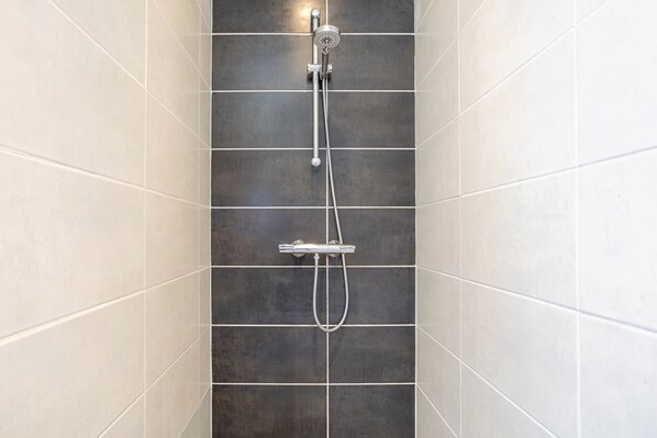 A shower with a handheld showerhead and a handheld hose, set against a tiled wall with a grid pattern.