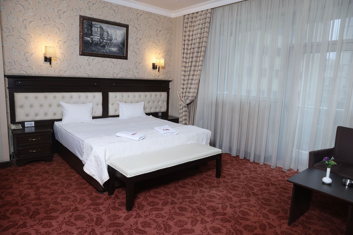 A hotel room with a large bed, two bedside tables, a nightstand, a desk, and a chair.
