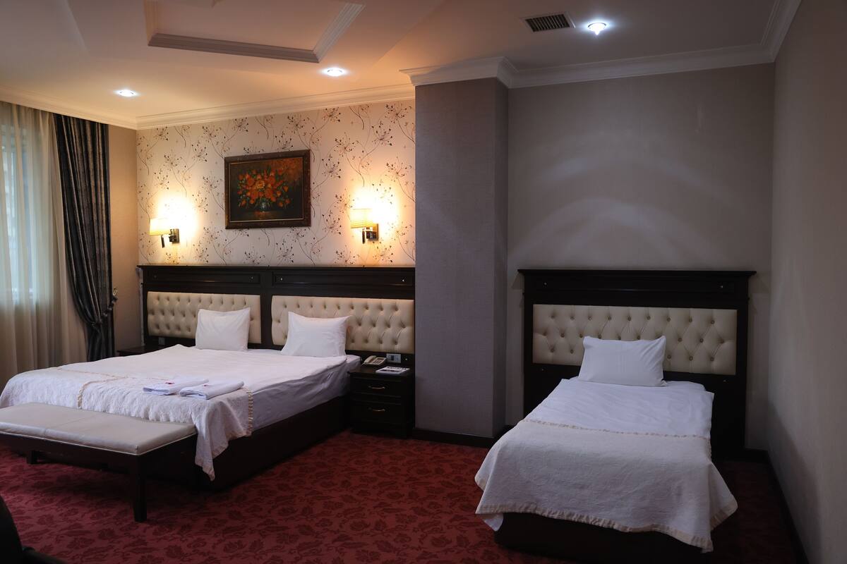 A hotel room with two beds, a red carpet, a painting on the wall, and two wall-mounted lamps.