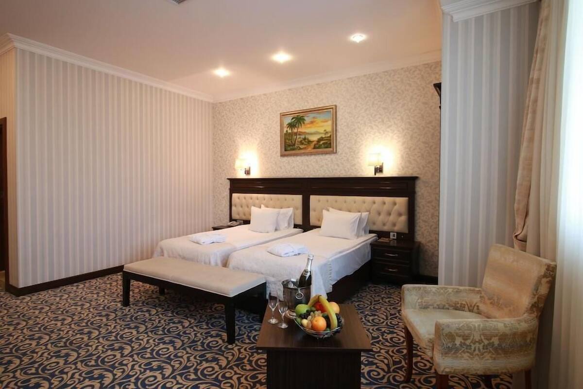 A hotel room with two beds, a sitting area, a fruit bowl, and a painting on the wall.