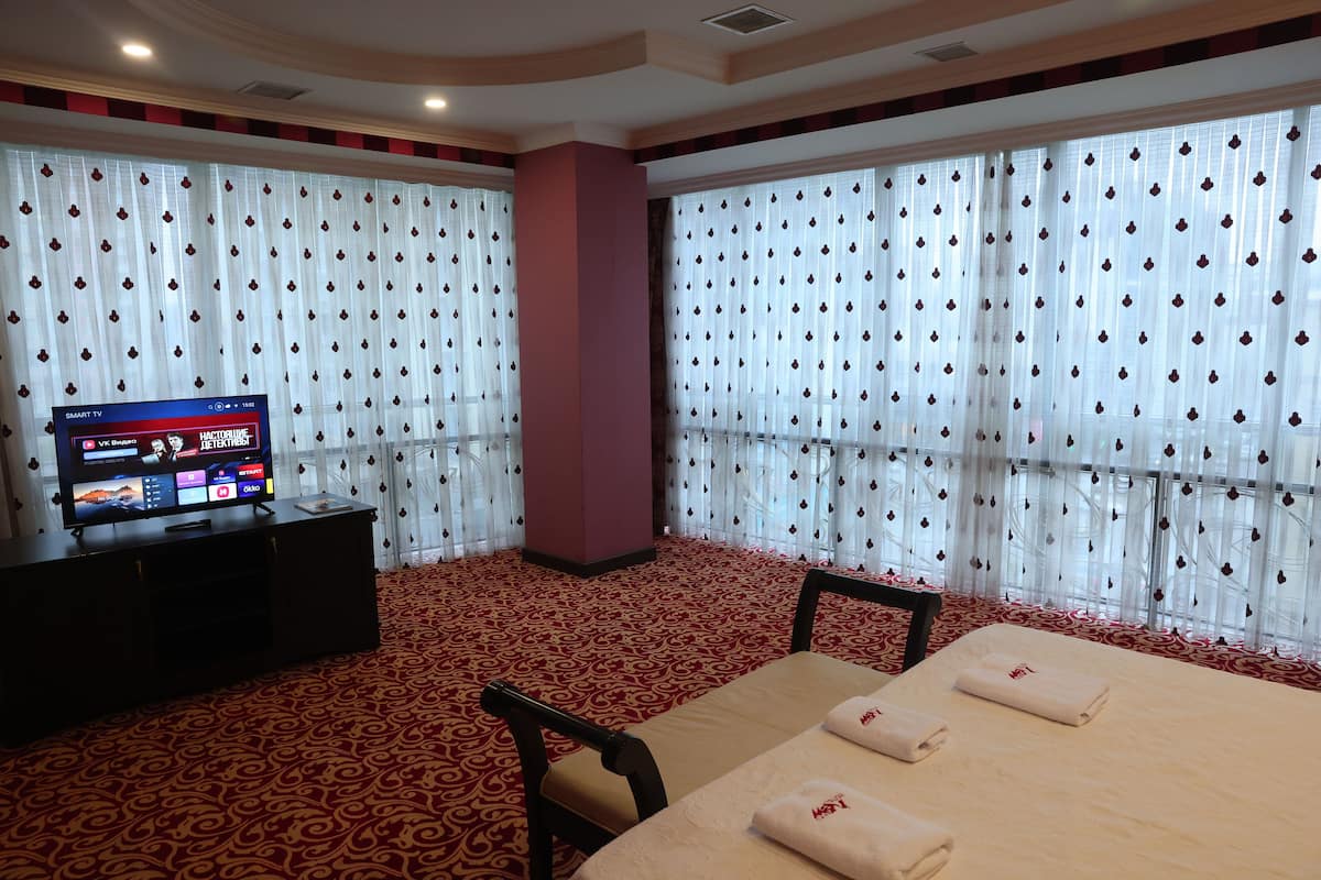 A hotel room with a TV on a stand, two beds, a desk, and curtains with a diamond pattern.