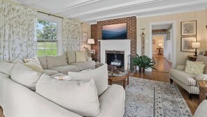 A spacious living room with a large sofa set, a fireplace, and a view of a green landscape through the windows. - Wine Country Farmhouse (Culpeper)