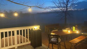 A wooden deck with a white railing, a table, chairs, and string lights. - Wine Country Farmhouse (Culpeper)