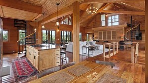 A spacious wooden cabin interior with a central island, a staircase, and a cozy living area. - The Houses at Lumusa (Culpeper)