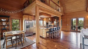 A spacious wooden cabin with a dining area, kitchen, and living room. - The Houses at Lumusa (Culpeper)