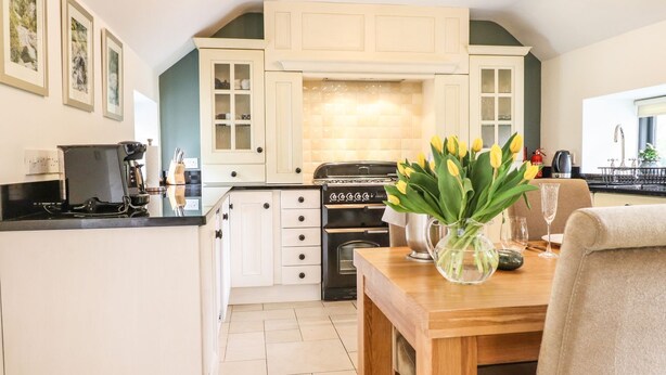 Una cocina moderna con armarios blancos, una estufa negra y un comedor con mesa y sillas de madera.
