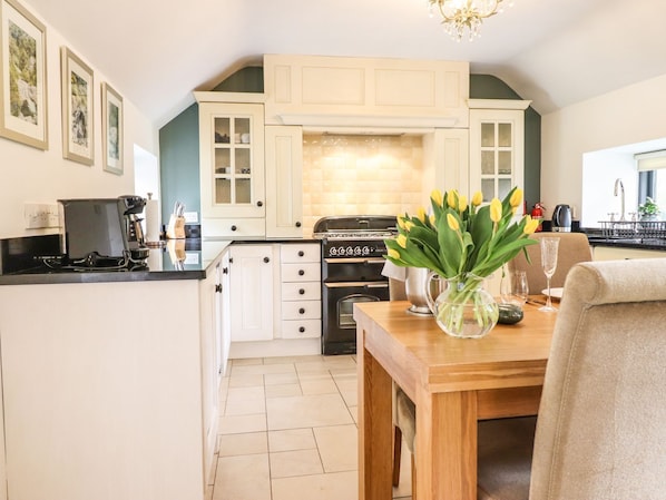 A modern kitchen with white cabinetry, a black stove, and a dining area with a wooden table and chairs. - The Talkhouse Cottage (Caersws)