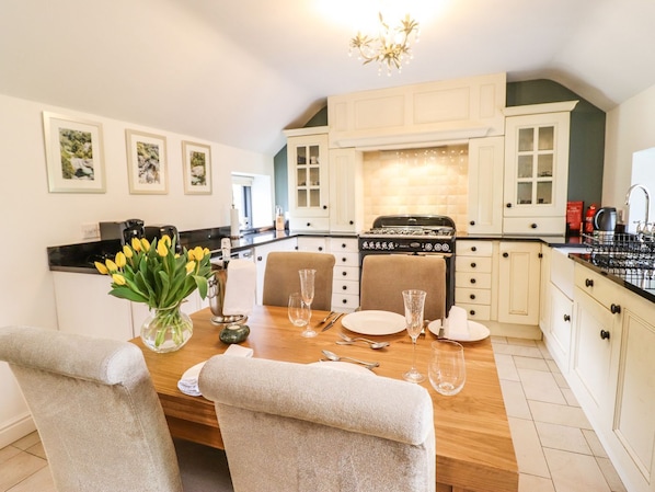 Een moderne keuken met witte kasten, een zwarte kookplaat en een eethoek met een houten tafel voor vier personen.