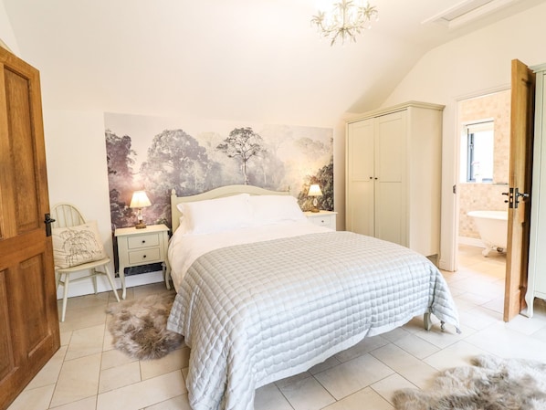 A bedroom with a large bed, two bedside tables with lamps, a wardrobe, and a bathroom visible through an open door. - The Talkhouse Cottage (Caersws)