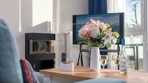A modern living room with a fireplace, a flat-screen TV, a wooden coffee table, a vase with flowers, and two glasses of white wine. - Luv & Lee BalticLoft - loft character meets Baltic Sea flair with sauna & fireplace (Zingst)
