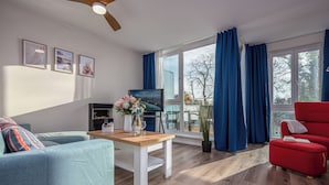 A modern living room with a wooden coffee table, a red armchair, a blue sofa, and a TV on a stand. - Luv & Lee BalticLoft - loft character meets Baltic Sea flair with sauna & fireplace (Zingst)