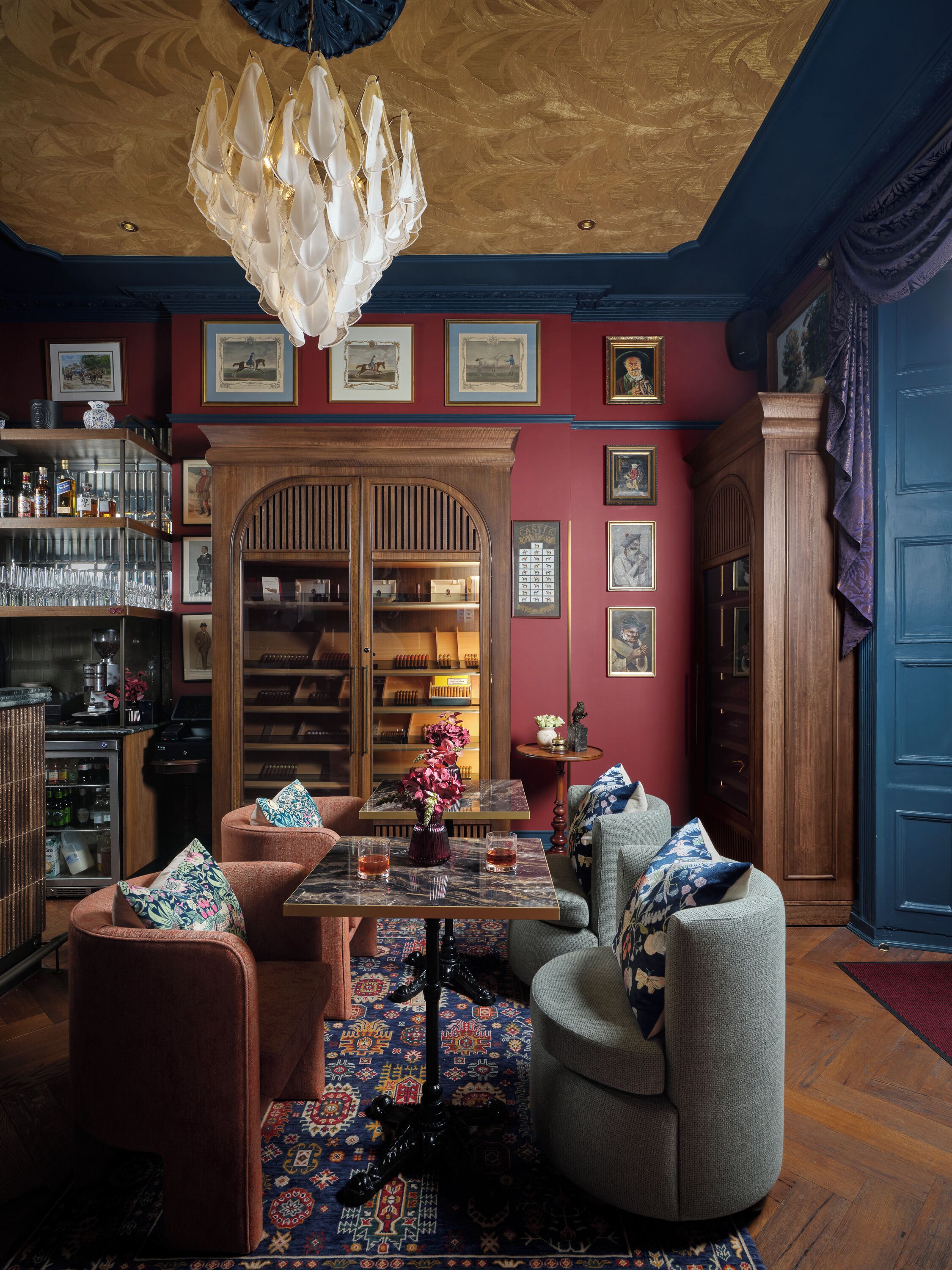 Una habitación con techo de madera, una araña, una zona de bar con estanterías, una mesa con sillas y una alfombra estampada.
