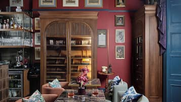 Una habitación con techo de madera, una araña, una zona de bar con estanterías, una mesa con sillas y una alfombra estampada.