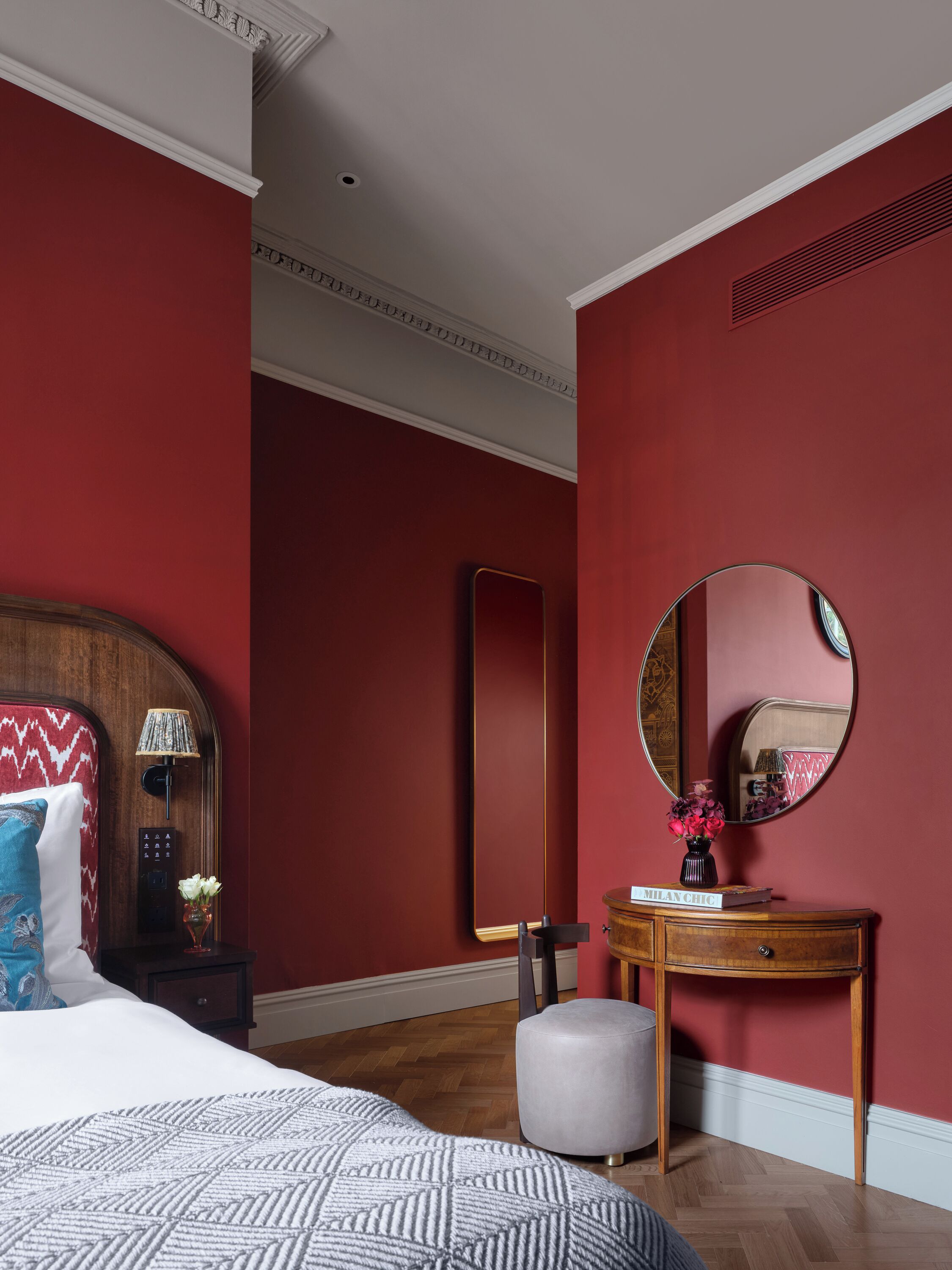 Quarto com cama, mesa de cabeceira, penteadeira, espelho e parede vermelha.