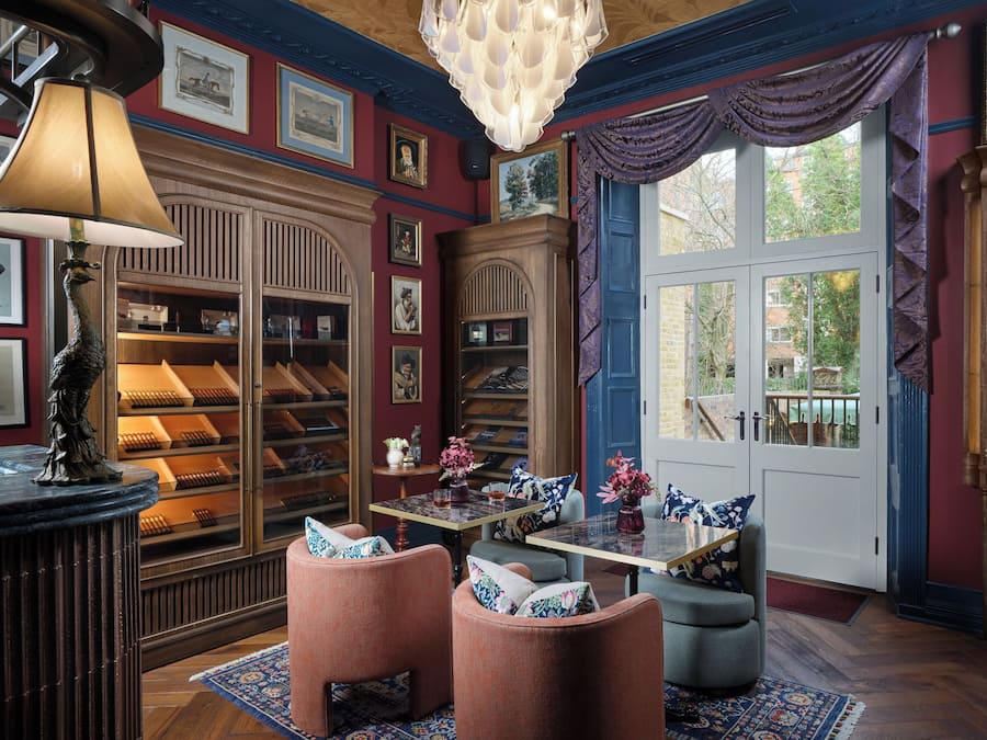 A library with bookshelves, a table with chairs, and a large window with curtains.