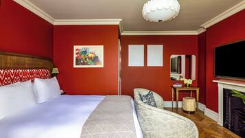 A hotel room with a large bed, a sofa, a TV, a fireplace, and a painting on the wall.