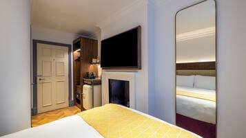 Habitación de hotel con cama, televisión montada en la pared, chimenea y puerta que da a un baño.