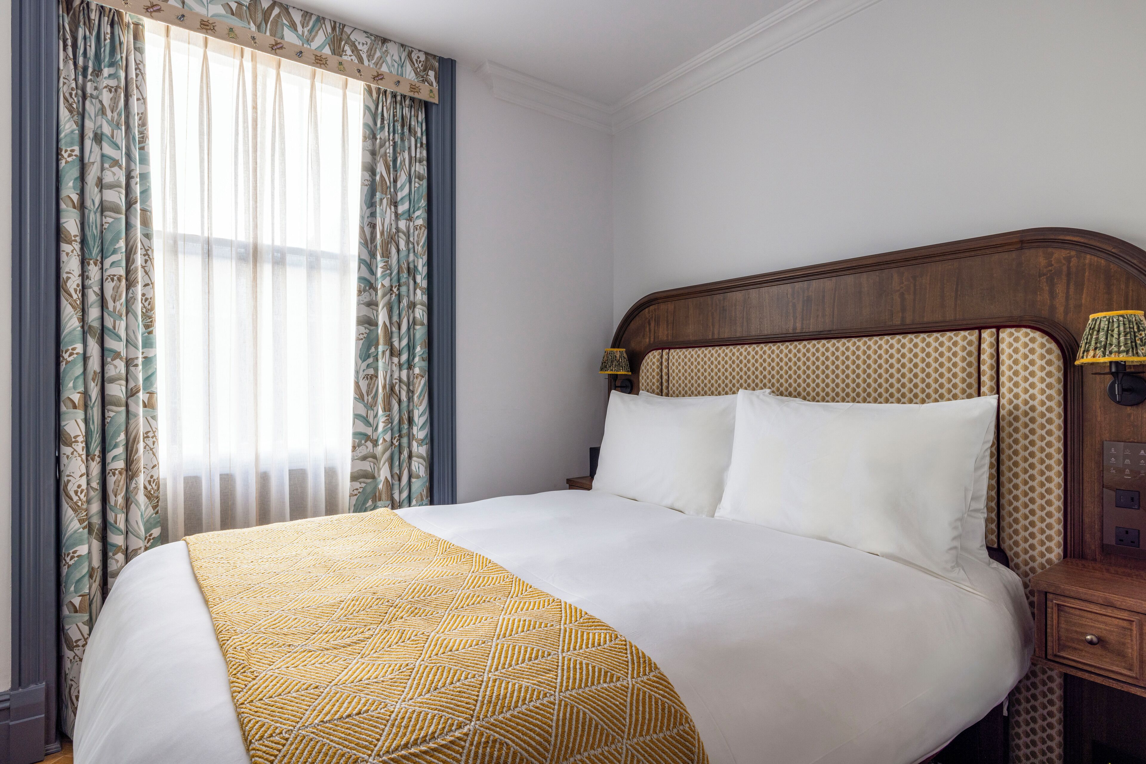 A neatly made bed with a patterned bedspread, a wooden headboard, and a nightstand with a lamp.
