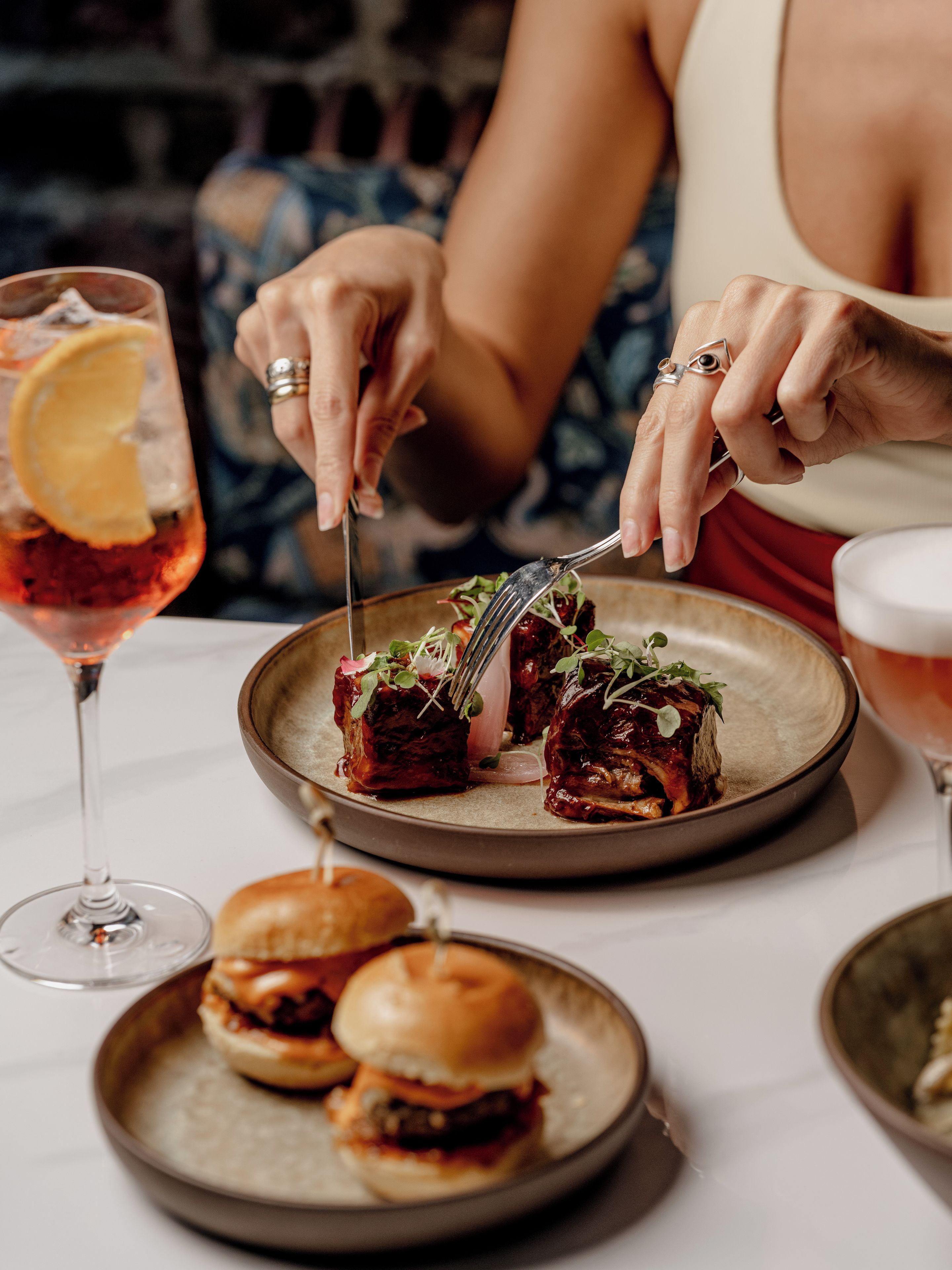 A dining table with a plate of food, a glass of drink, and a burger.